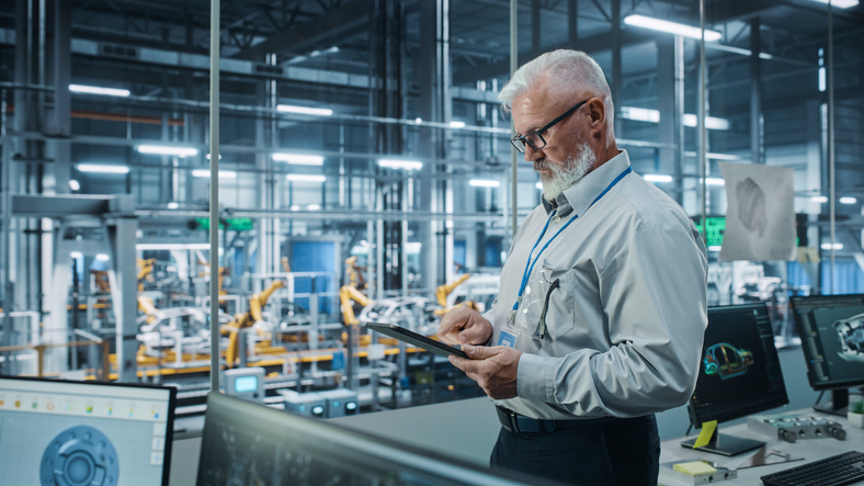 Senior engineer reviewing data on a tablet inside an advanced manufacturing facility